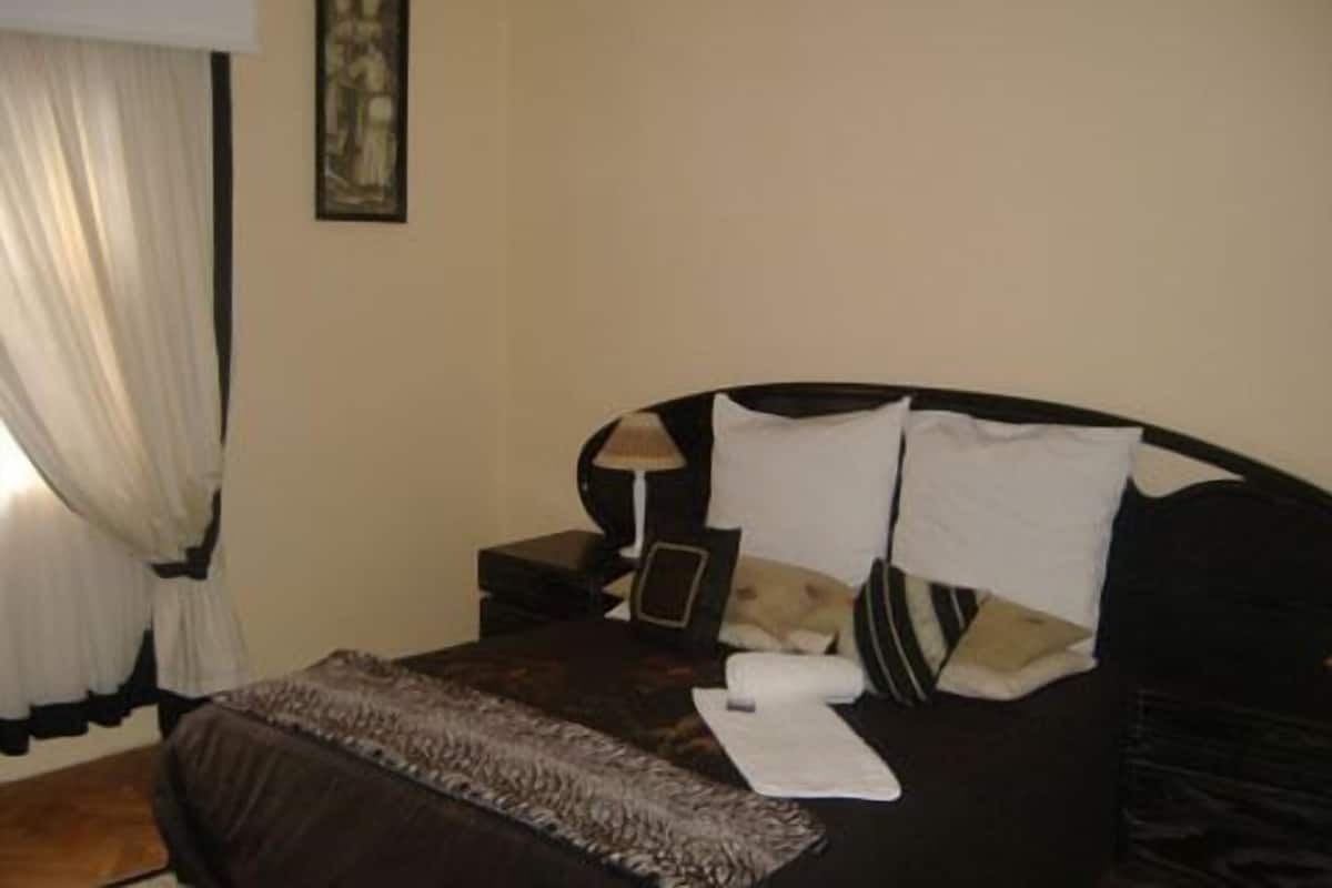A neatly made bed with a dark brown bedspread, two pillows, and a small bedside table with a lamp.