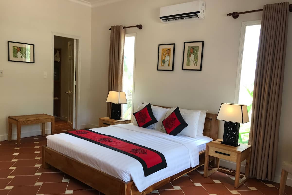 A hotel room with a large bed, two bedside tables with lamps, a wooden bench, and a door leading to a closet.