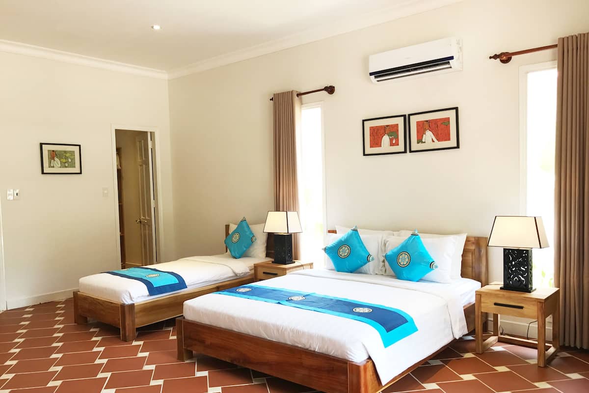 A hotel room with two beds, a wooden floor, a ceiling fan, and a window with curtains.