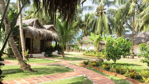 A tropical garden with a thatched-roof building, palm trees, and a tiled pathway. - Peppercorn Beach (Phu Quoc)