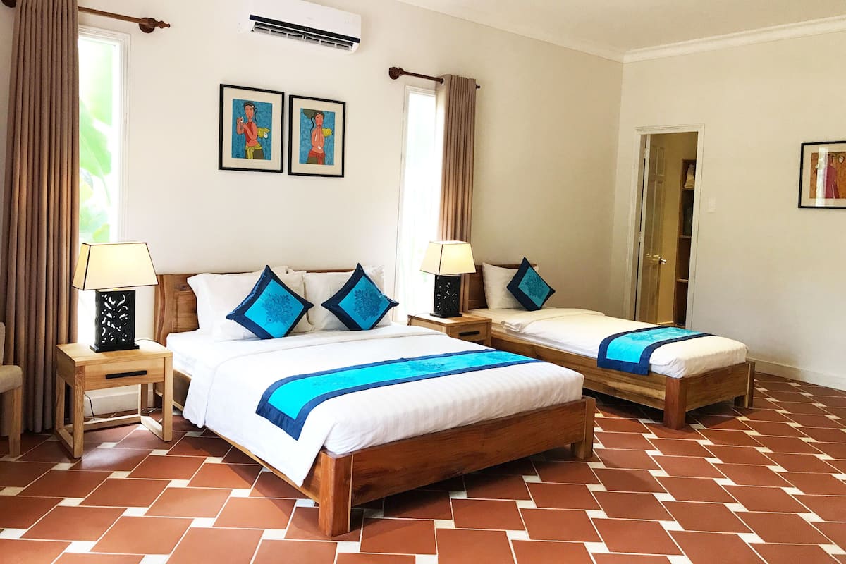 A hotel room with two single beds, a wooden floor, a ceiling fan, and a window with curtains.
