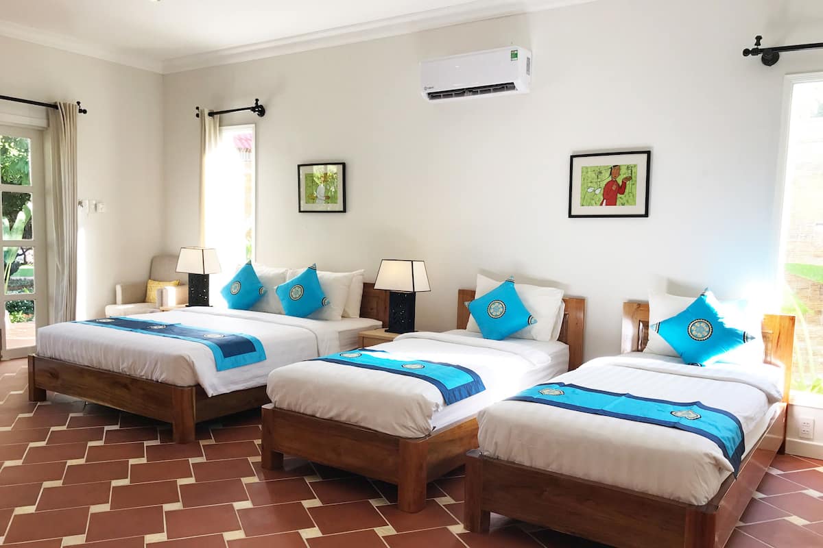 A hotel room with three wooden beds, each with blue and white bedding, and a tiled floor.