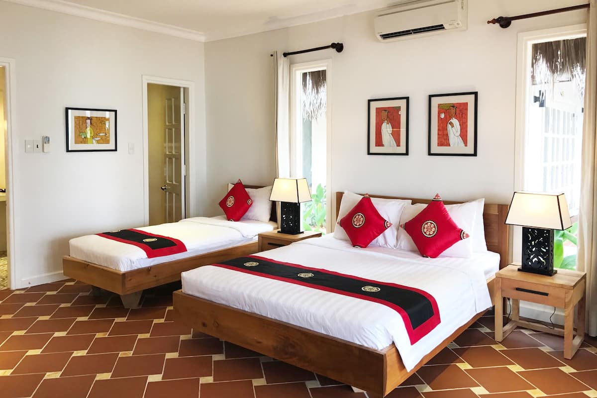 A hotel room with two beds, a wooden floor, a window with curtains, and a wall-mounted air conditioner.