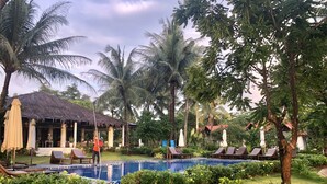 A pool area with lounge chairs, a thatched-roof building, and lush greenery. - Peppercorn Beach (Phu Quoc)