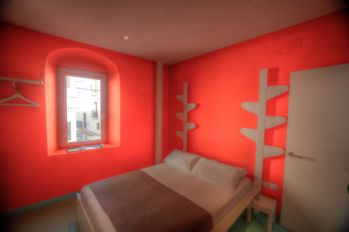 Un dormitorio con cama, ventana, armario y perchero en la pared.