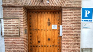 Una puerta de madera con remaches de metal, una pequeña placa encima y una señal de estacionamiento a la derecha.