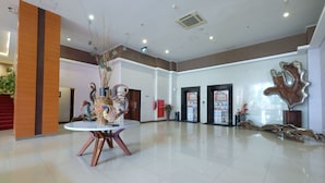 Um hall amplo com uma mesa redonda, um balcão de recepção e uma grande escultura abstrata.