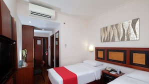 Quarto de hotel com duas camas, televisão, secretária e uma obra de arte na parede.