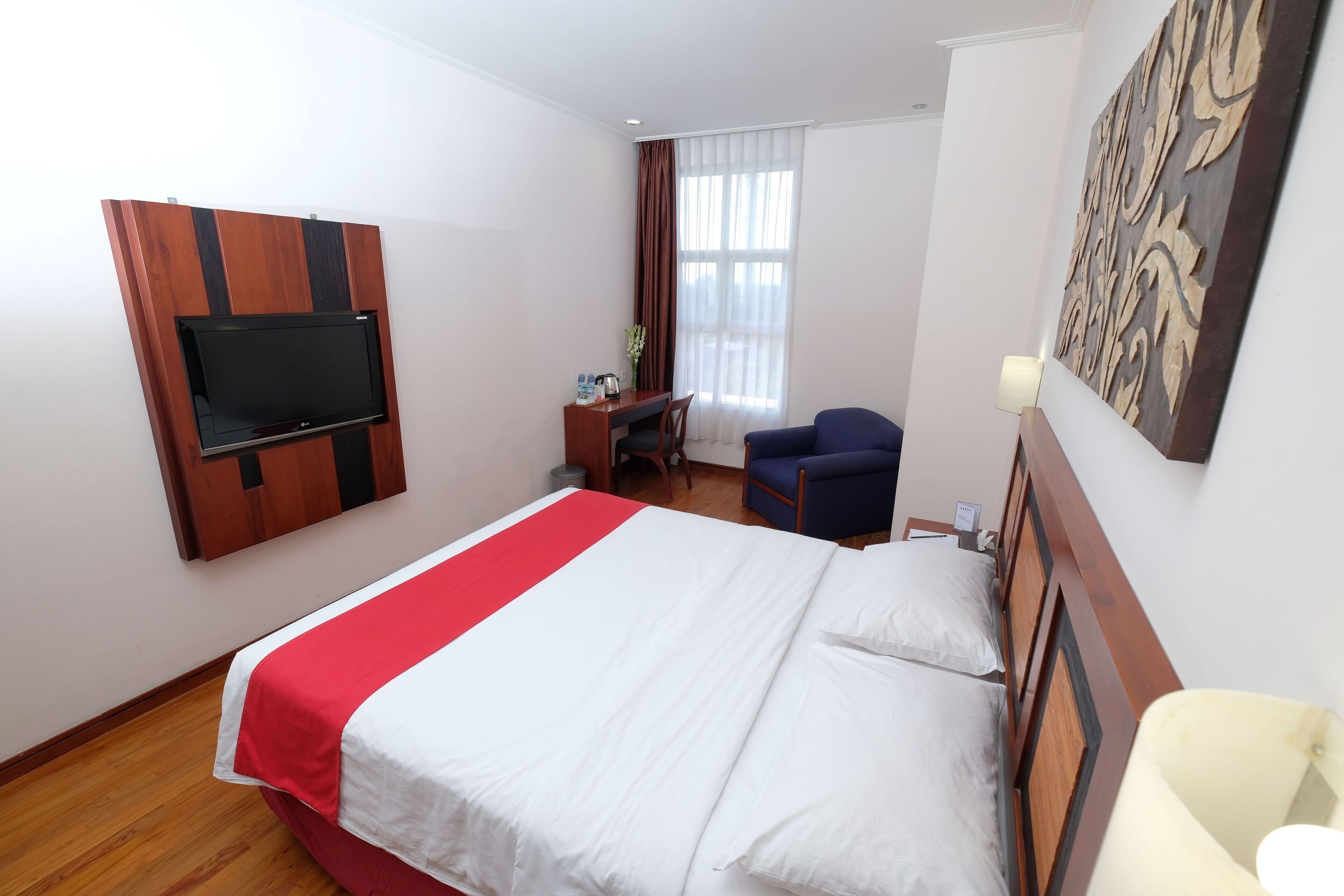 A hotel room with a bed, a desk, a chair, a TV, and a decorative wall piece.
