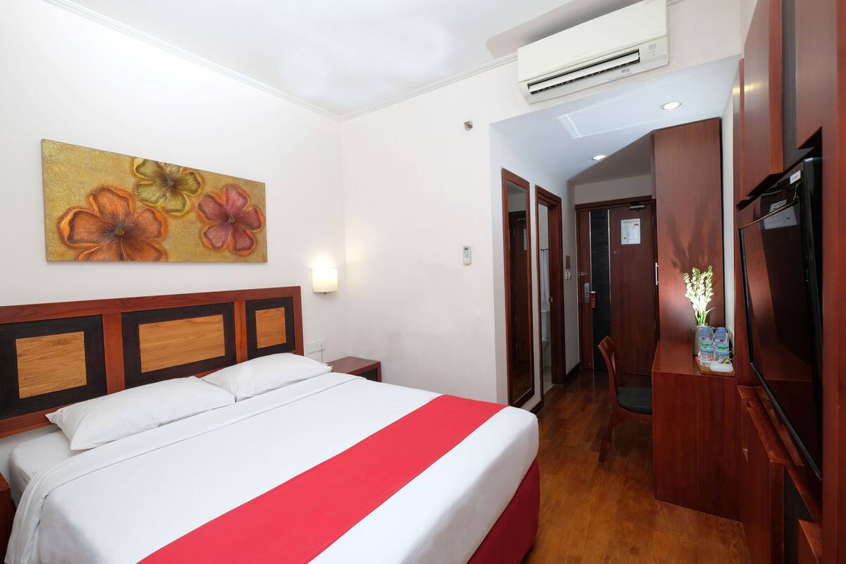A hotel room with a bed, a desk, a chair, and a painting on the wall.