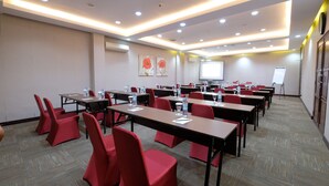 Sala de conferências com várias mesas e cadeiras vermelhas, equipada com garrafas de água e blocos de notas.