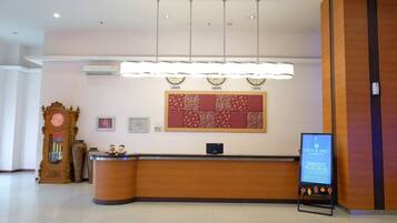 Zona de recepción de hotel con un mostrador de madera, un reloj de pared, un certificado enmarcado y un panel de anuncios digital.