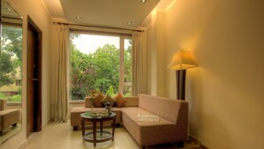 A living room with a sofa, a coffee table, a lamp, and a view of greenery outside. - Hotel Regent Intercontinental (New Delhi)