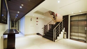 A modern interior with a staircase, an elevator, and a long corridor. - Hotel Regent Intercontinental (New Delhi)