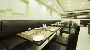 A restaurant with long tables, black leather booths, and a modern interior design. - Hotel Regent Intercontinental (New Delhi)