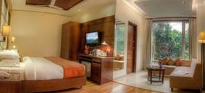 A hotel room with a bed, a desk with a TV, a sofa, and a view of greenery. - Hotel Regent Intercontinental (New Delhi)