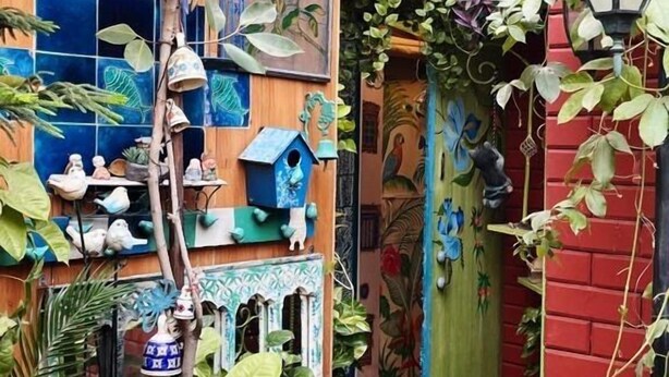 A narrow alleyway with wooden walls, hanging birdhouses, and lush green plants. - On The House - Bed and Breakfast (New Delhi)