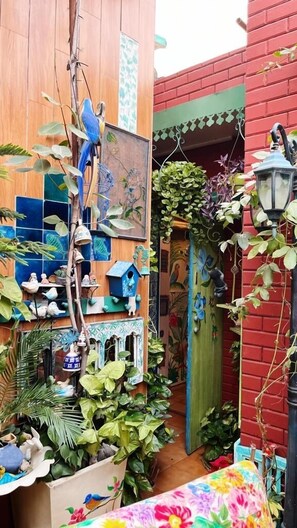 A narrow alleyway with wooden walls, hanging birdhouses, and lush green plants. - On The House - Bed and Breakfast (New Delhi)