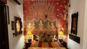 A bed with a patterned bedspread, two bedside lamps, and a tapestry with a central figure on the wall. - On The House - Bed and Breakfast (New Delhi)