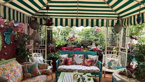 A covered patio area with a striped canopy, a sofa with colorful cushions, and various potted plants. - On The House - Bed and Breakfast (New Delhi)