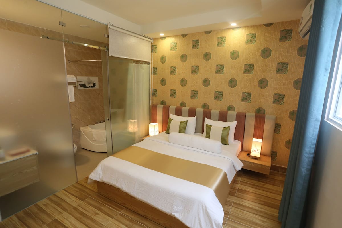 A hotel room with a bed, bedside lamps, a glass shower enclosure, and a patterned wall.