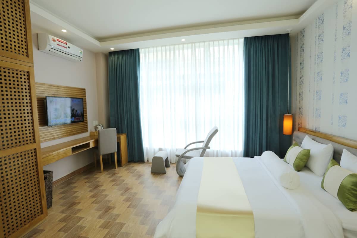 A hotel room with a bed, a desk, a chair, a television, and a large window with curtains.