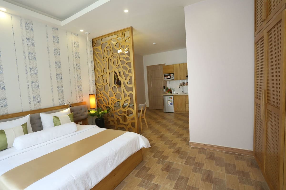 A hotel room with a bed, a desk, a chair, a small kitchenette, and a decorative partition.
