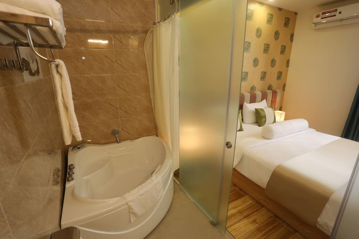 A modern hotel room with a bathtub, a bed with white bedding, and a shower area.