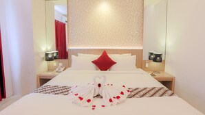 A hotel room with a neatly made bed, a red pillow, two bedside tables with lamps, and a wall with a patterned wallpaper. - Grand HAP Hotel (Surakarta)