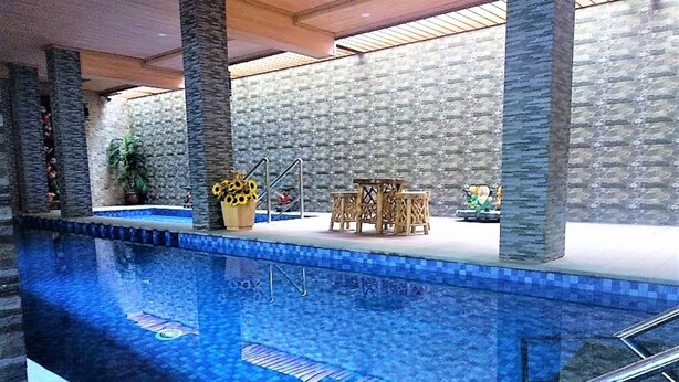 An indoor swimming pool with a tiled edge, stone pillars, and a seating area with a table and chairs. - Grand HAP Hotel (Surakarta)