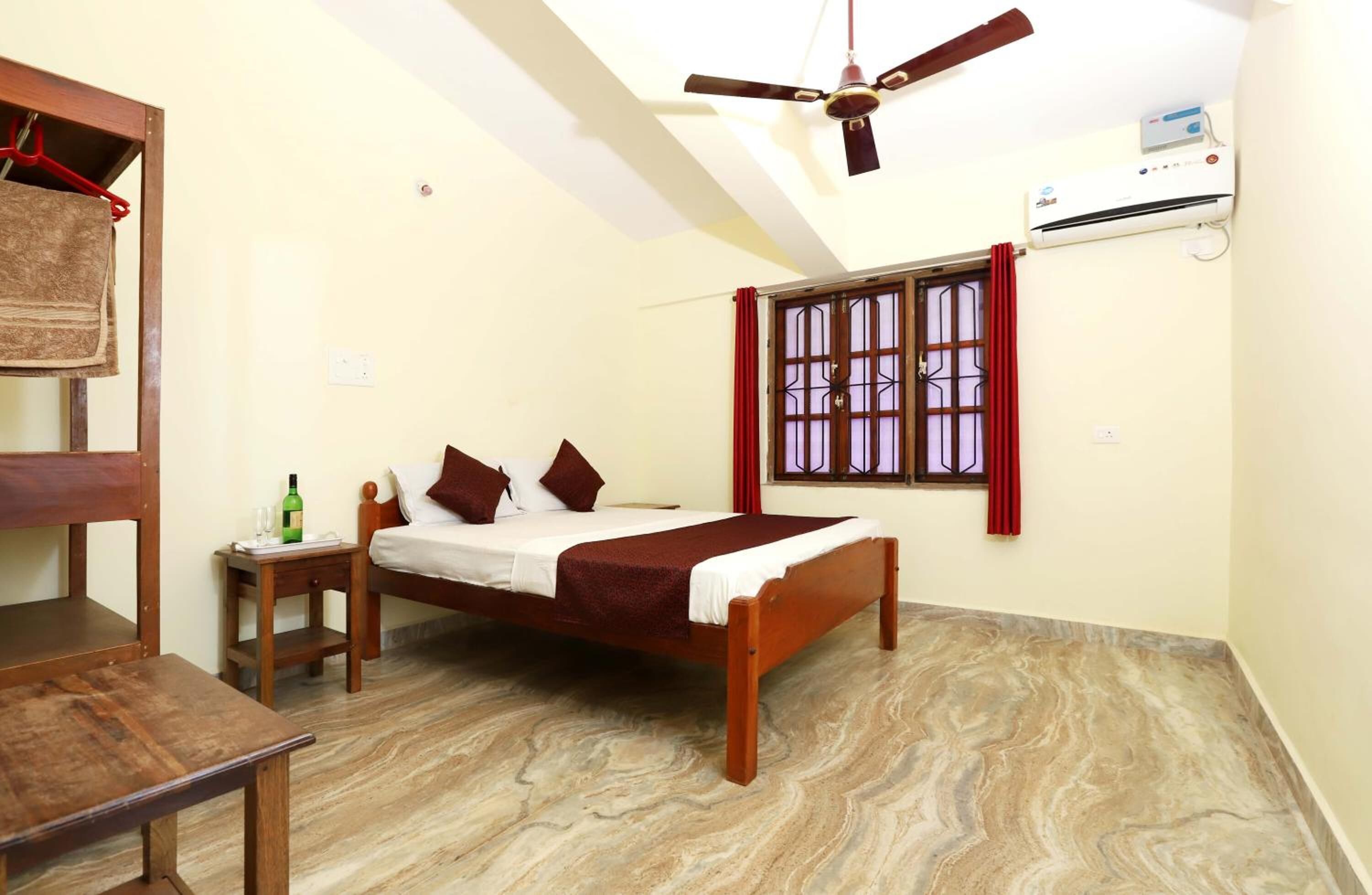 A bedroom with a bed, a wooden table, a hanging towel, a ceiling fan, and an air conditioning unit.