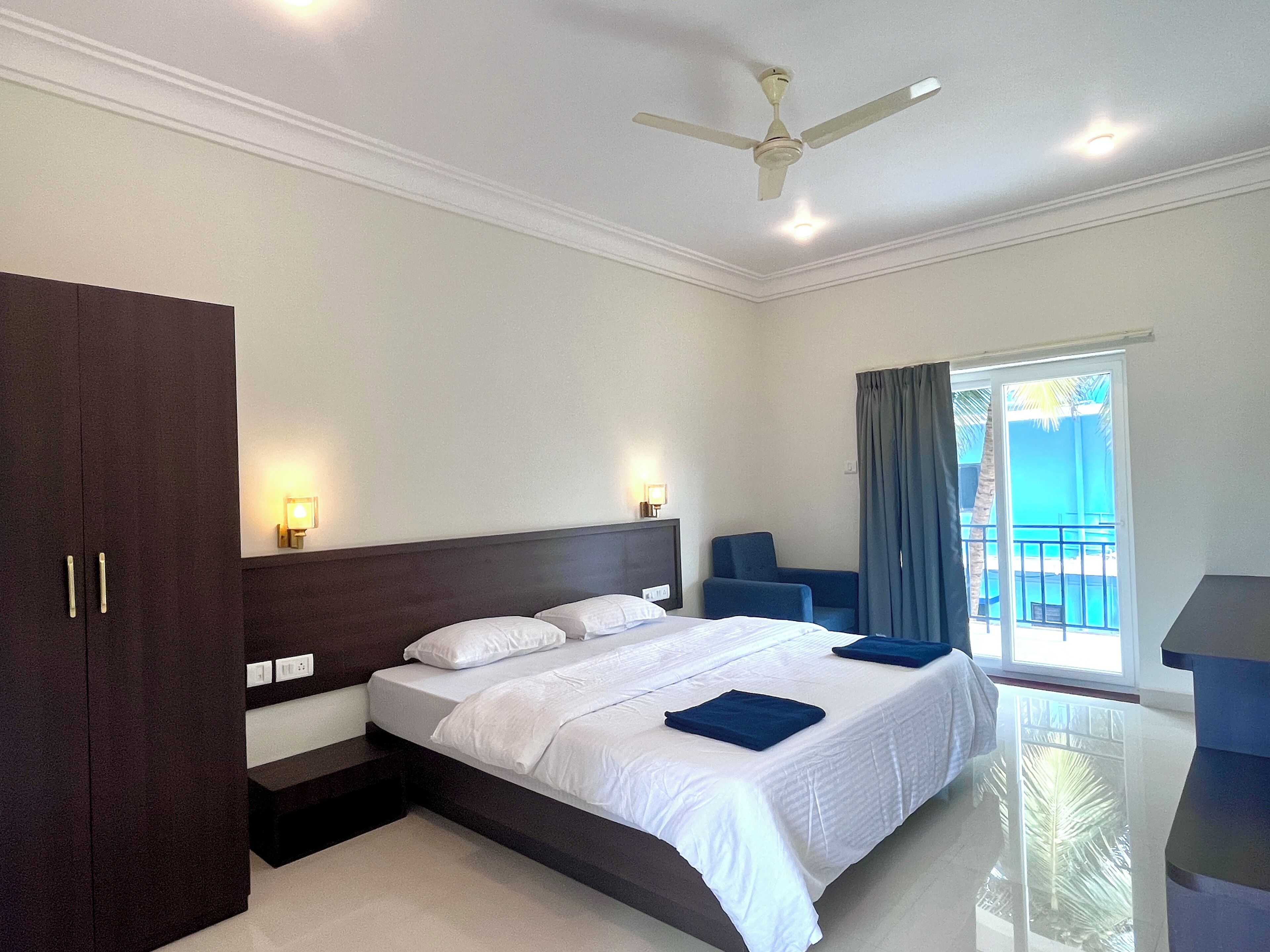 Ein Hotelzimmer mit Bett, Schreibtisch, Stuhl, Deckenventilator und Blick ins Freie.