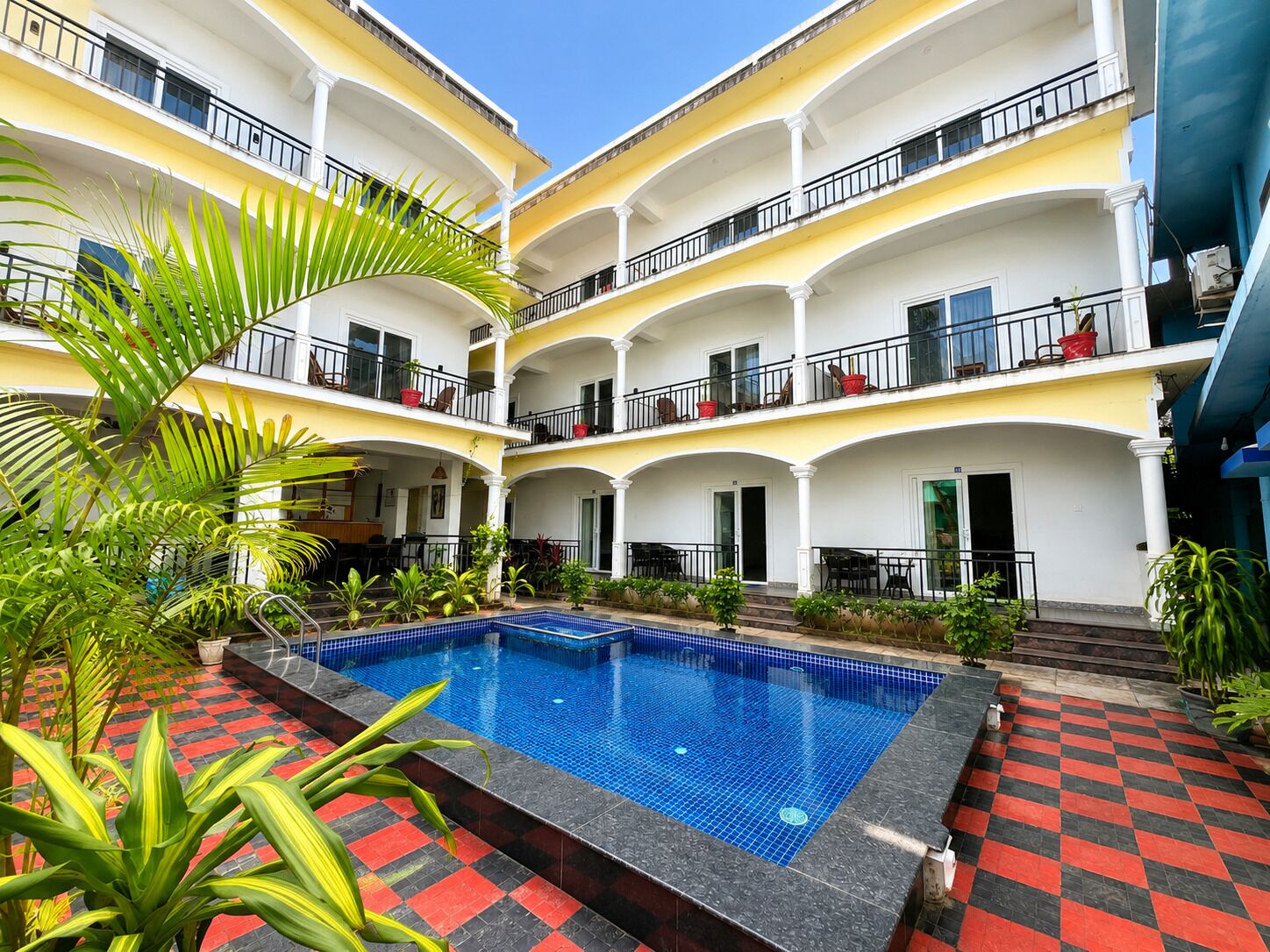 A multi-story hotel with a central pool surrounded by balconies and potted plants.