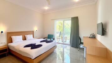 A hotel room with a bed, a desk, a chair, a television, and a balcony with a view of palm trees.