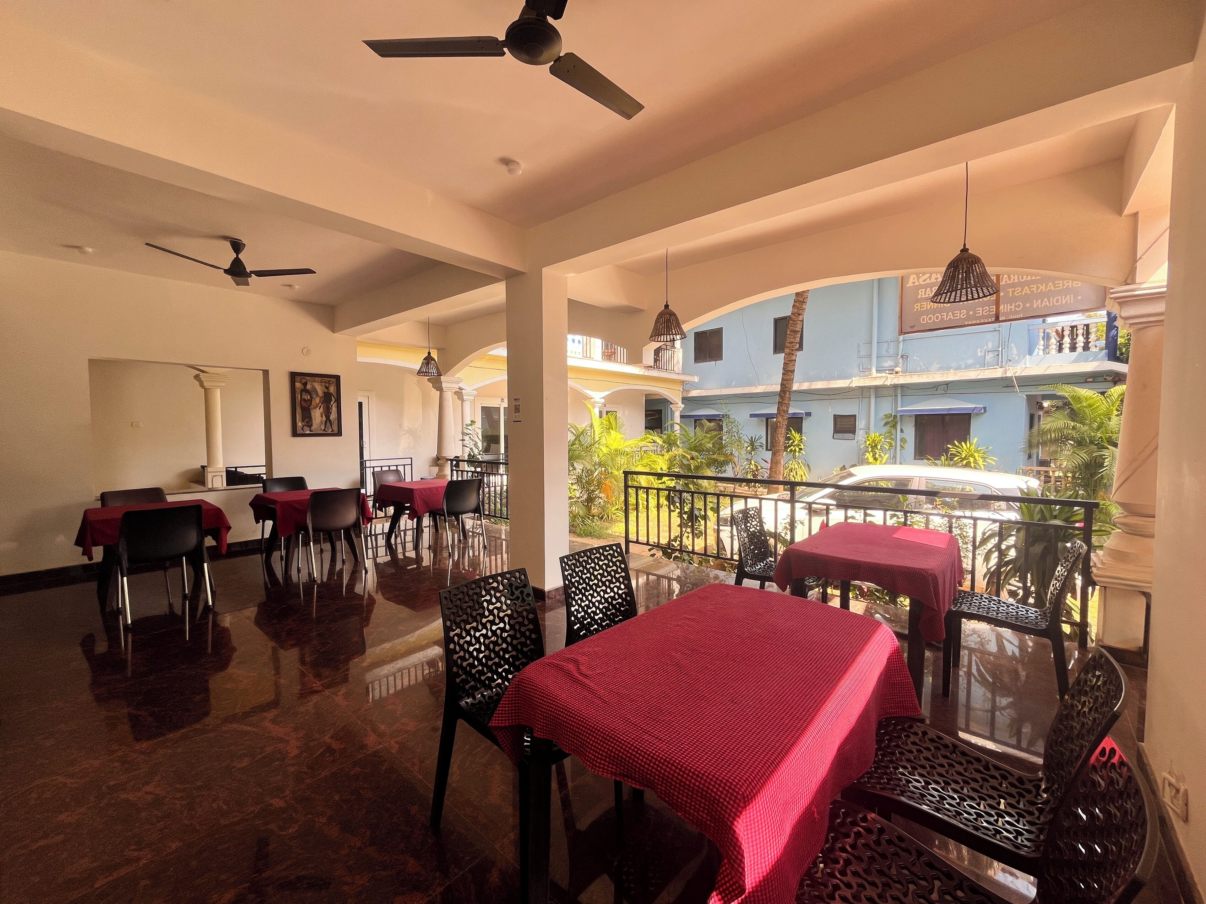 A restaurant with tables and chairs, a ceiling fan, and a view of buildings and greenery outside.