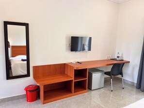A hotel room with a wooden desk, a television mounted on the wall, a small refrigerator, a trash bin, and a chair. - Morjim Sunset Hotel - 300 Meter to Morjim Beach with Pool & Kitchen Apartments (Morjim)
