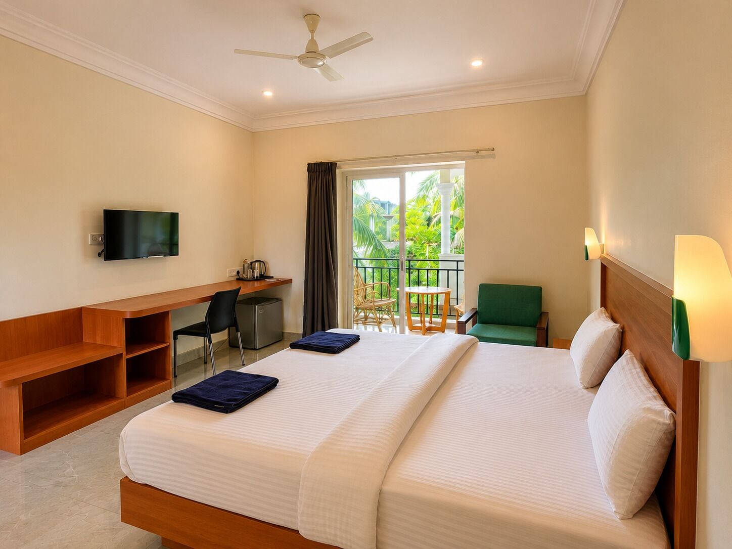 A hotel room with a bed, a desk, a television, a chair, and a balcony with a view of greenery.