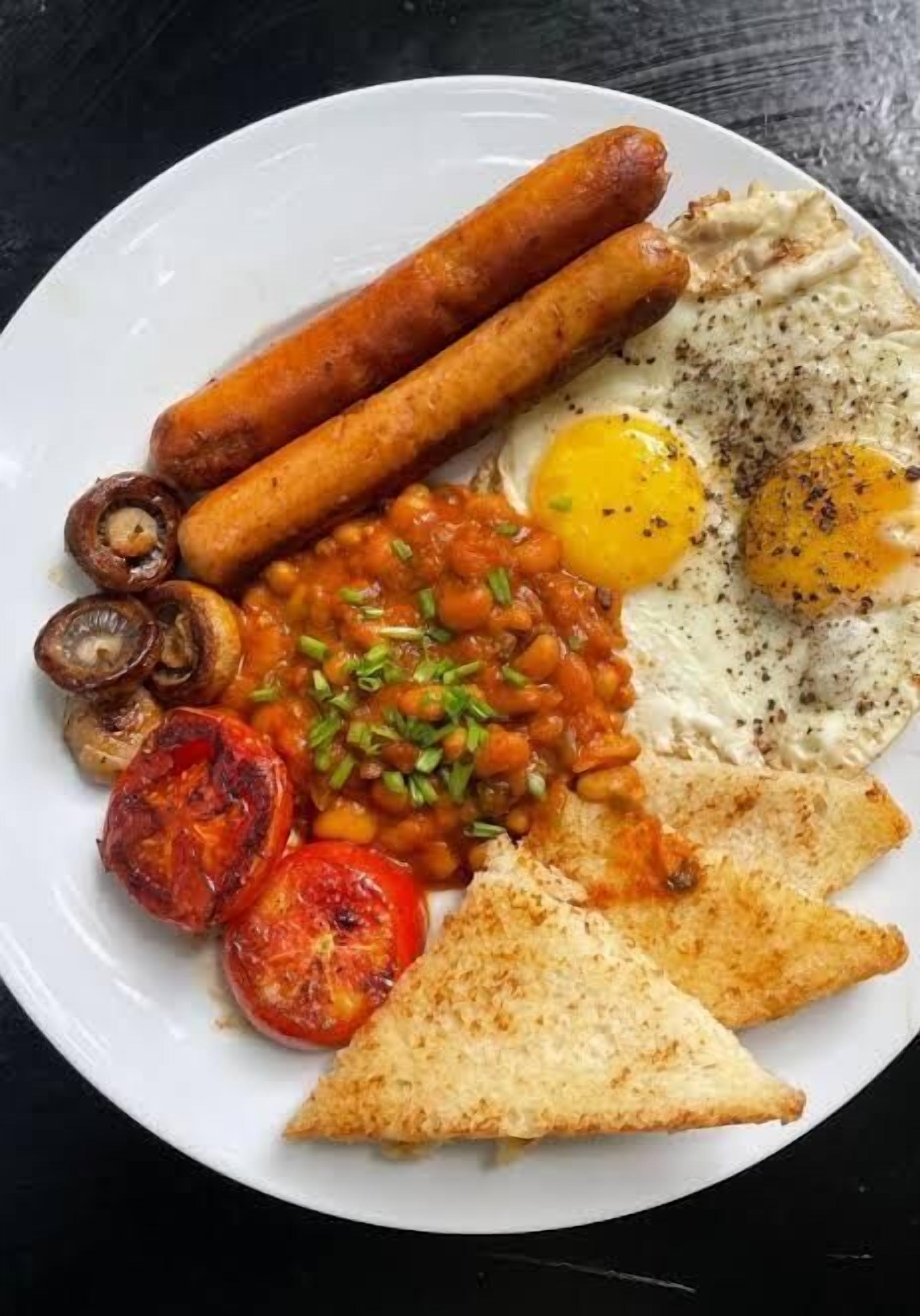 Een bord ontbijt met worstjes, eieren, bonen, champignons, tomaten en toast.