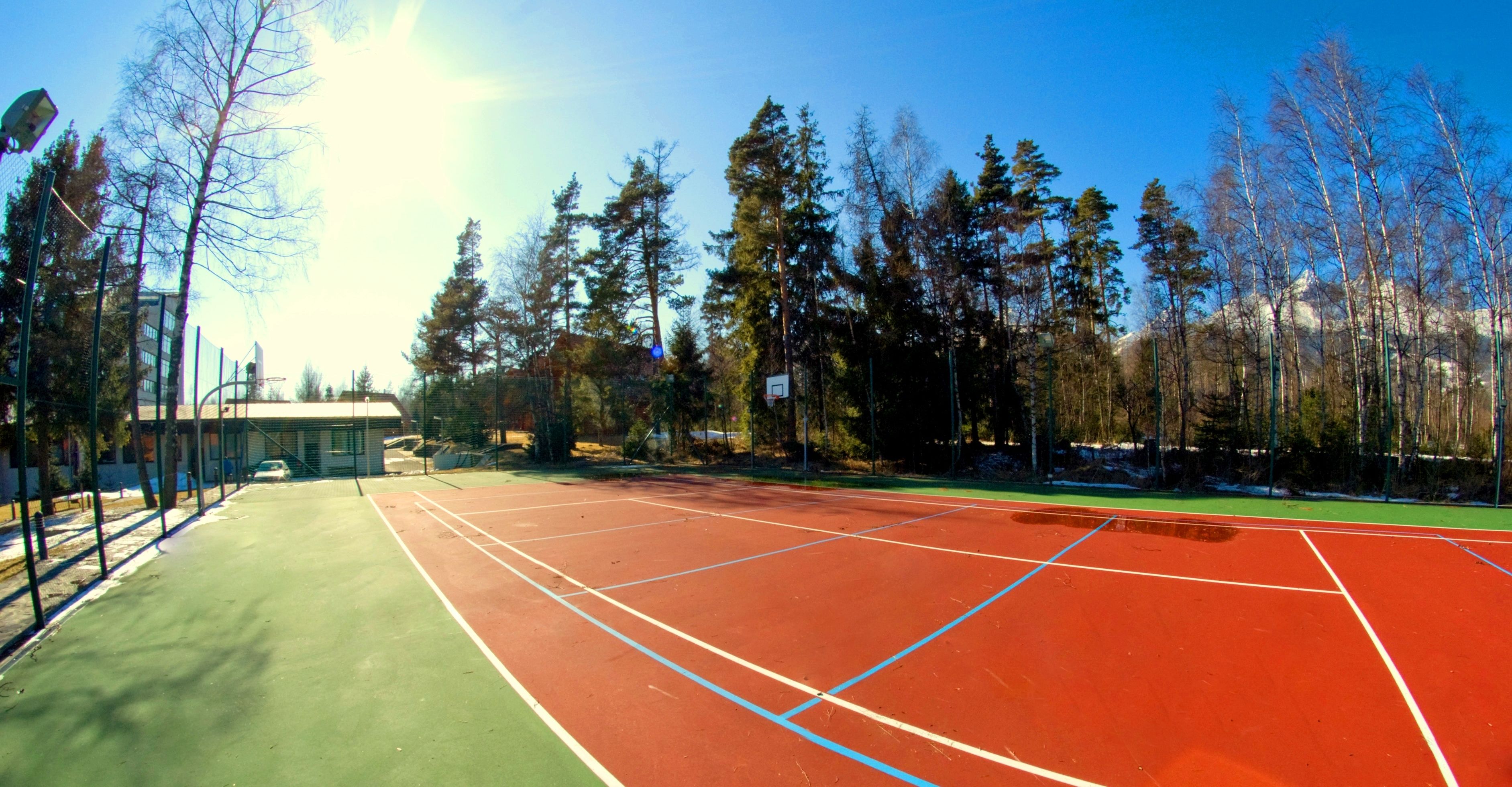 Un court de tennis à la surface verte et rouge, entouré d’arbres et avec un bâtiment visible à l’arrière-plan.