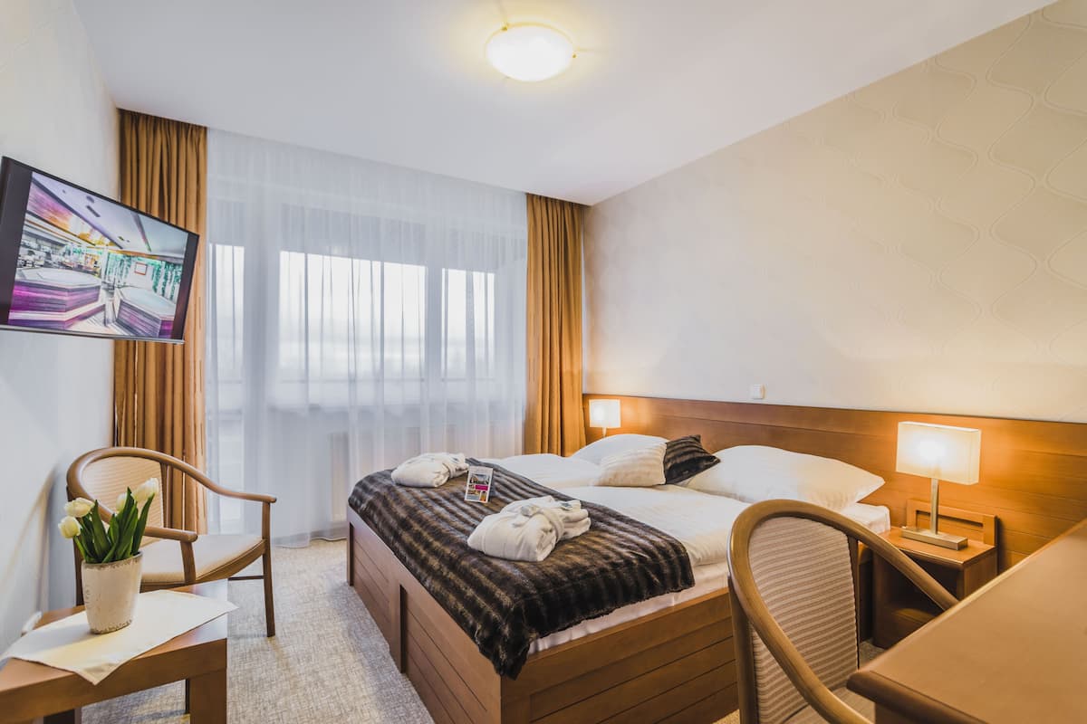 Habitación de hotel con cama, escritorio, silla, televisor y ventana con cortinas.