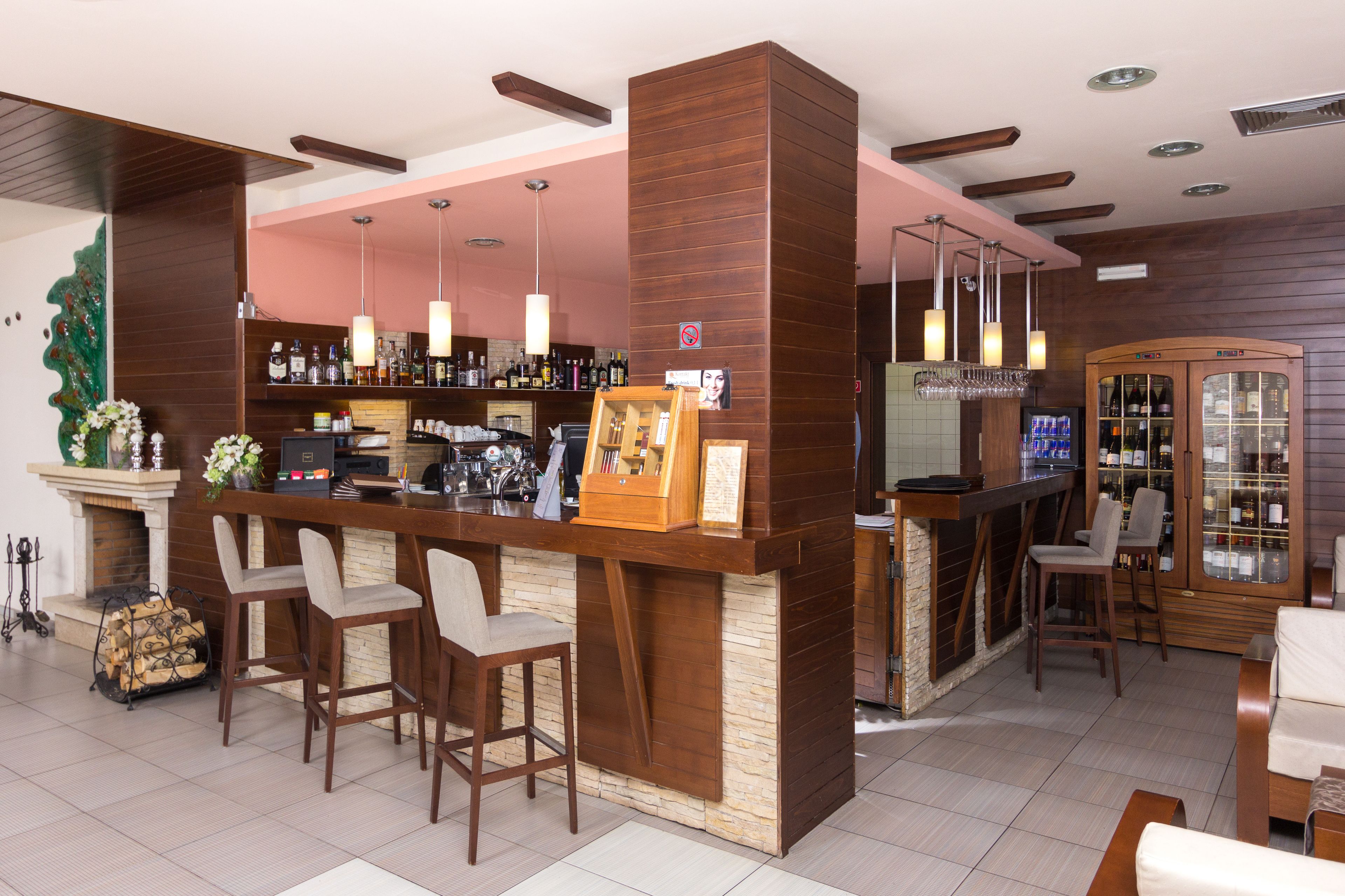 Een bar met houten toonbanken, barstoelen en hangende hanglampen.