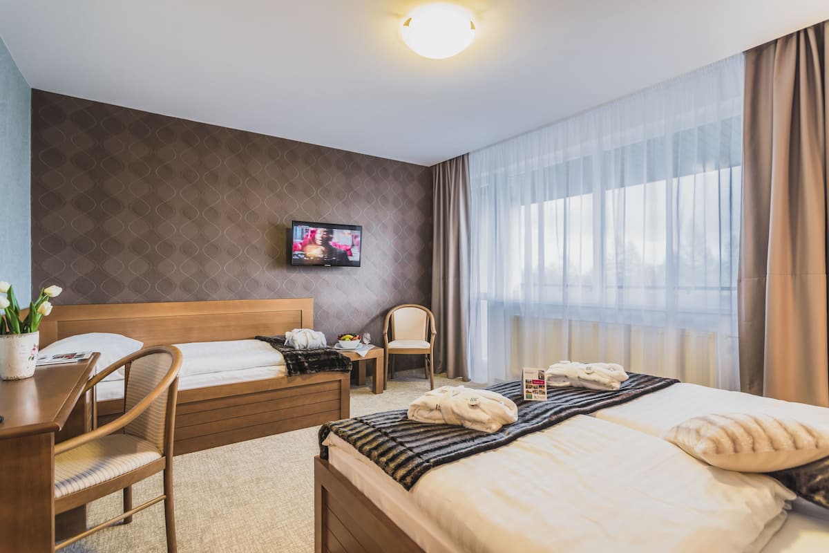 Habitación de hotel con cama de madera, un escritorio, una silla, televisor en la pared y ventana con cortinas.