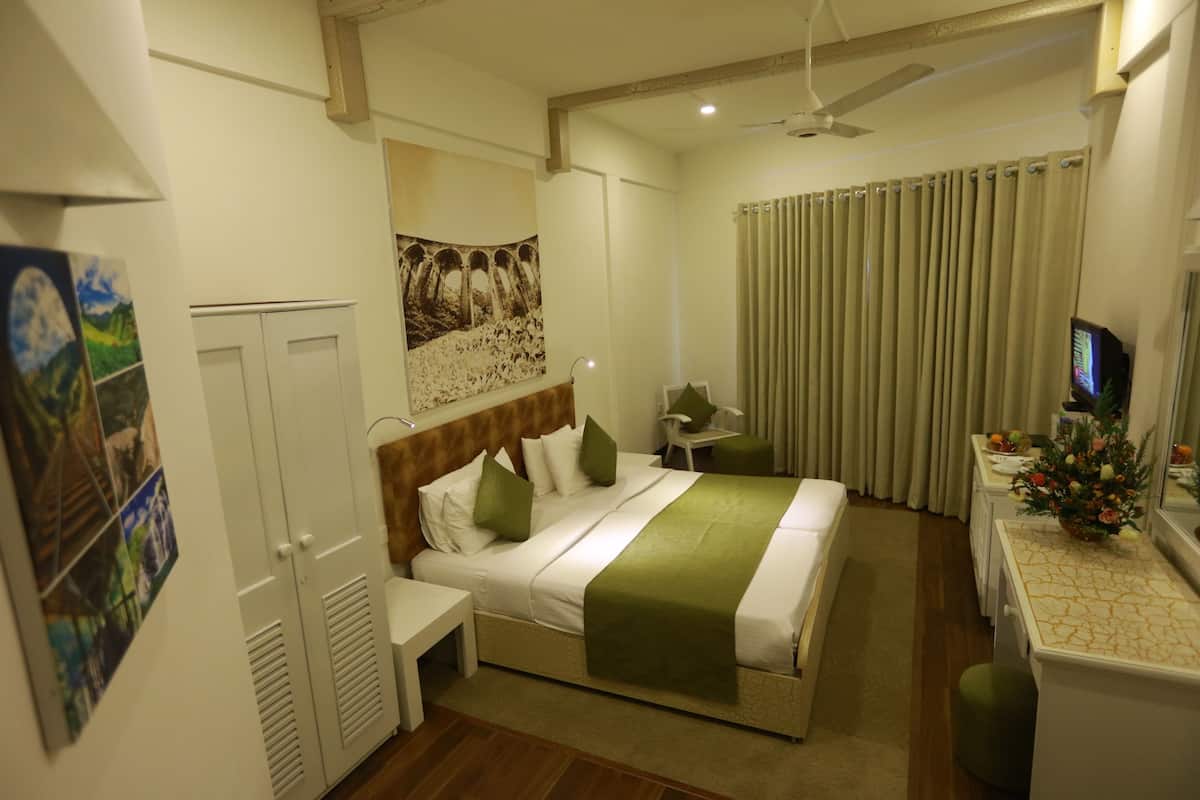 A hotel room with a bed, bedside table, a desk with a chair, a television, and a window with curtains.