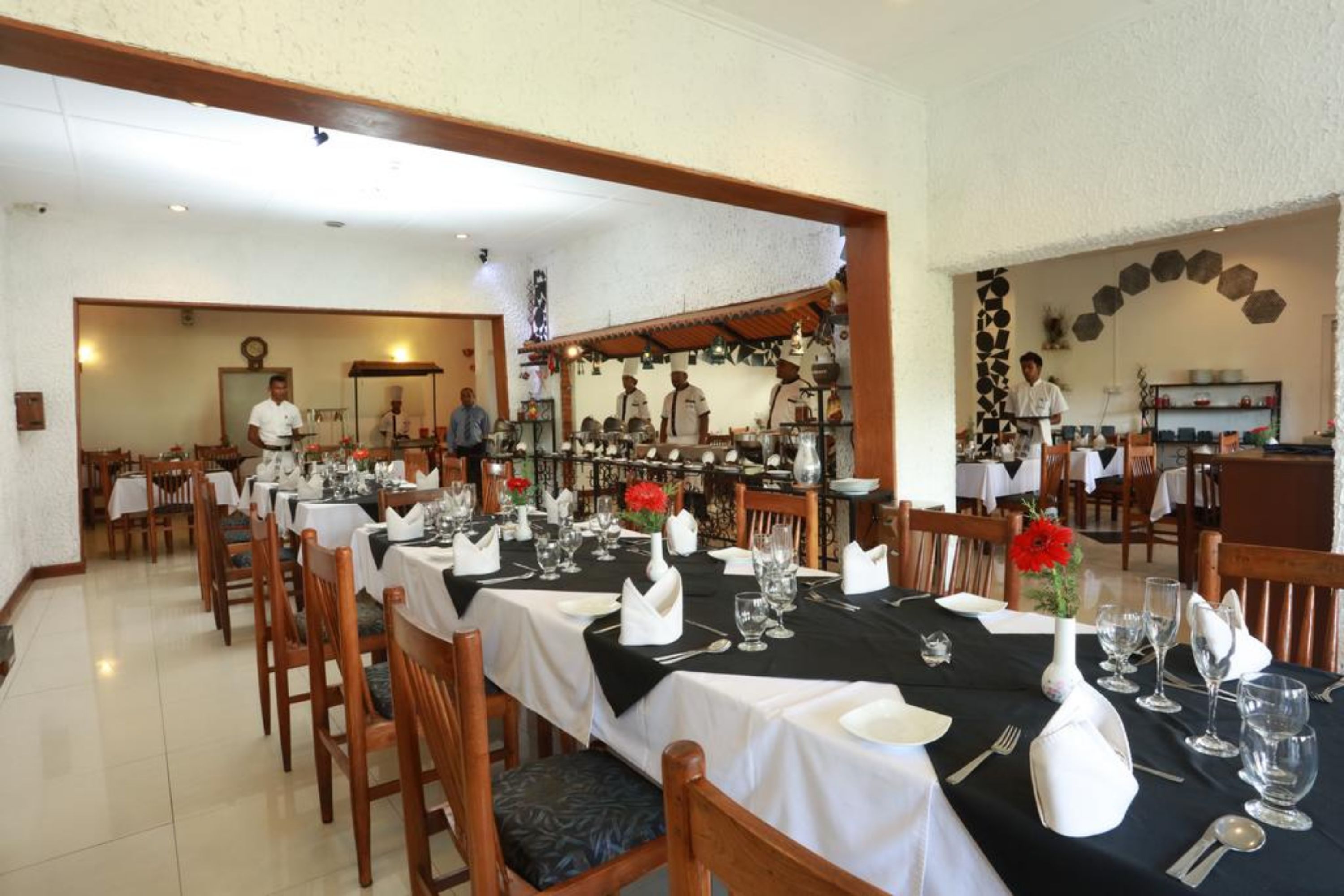 A restaurant with tables set for dining, a kitchen area, and a bar.