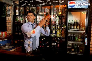 A bartender preparing a drink in a bar with a variety of alcohol bottles and a Pepsi refrigerator. - Orient Hotel (Bandarawela)