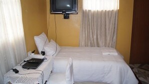 Ein Hotelzimmer mit Bett, Wand-Fernseher, Laptop und Nachttisch mit Lampe.