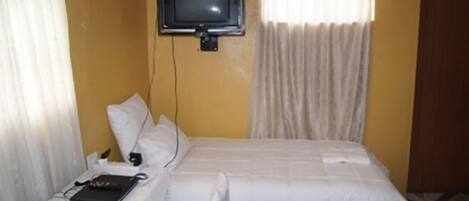 A hotel room with a bed, a television mounted on the wall, a laptop, and a bedside table with a lamp.