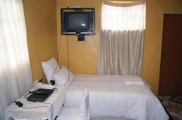 Une chambre d’hôtel avec un lit, un téléviseur fixé au mur, un ordinateur portable et une table de chevet avec une lampe.