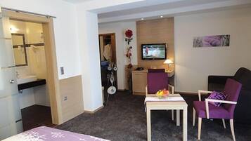 Ein Hotelzimmer mit Bett, Schreibtisch, Stuhl, Fernseher und einem durchgegangenen Tür sichtbaren Badezimmer.