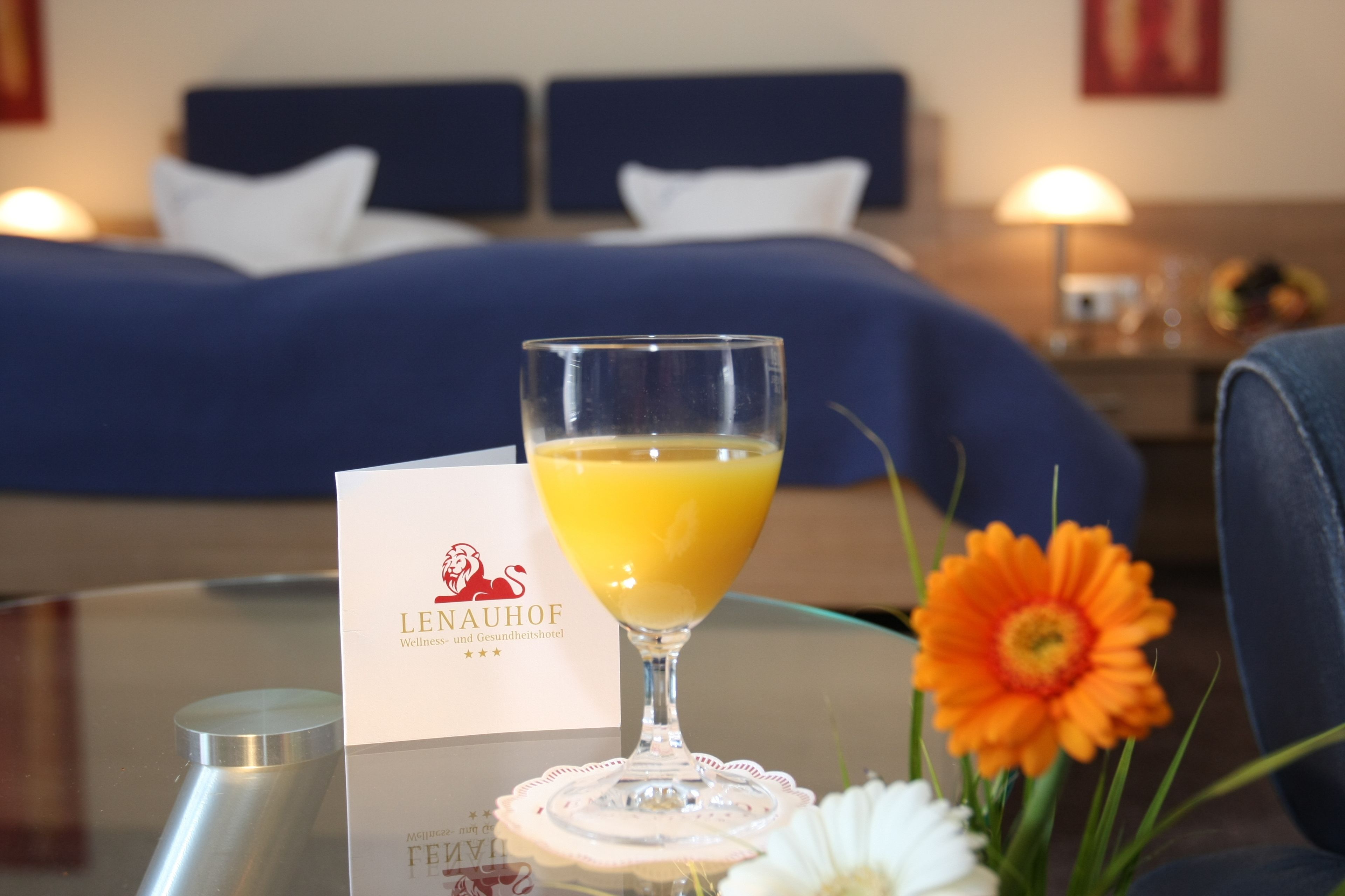 Una habitación de hotel con una cama, un vaso de jugo de naranja, una flor y un menú sobre la mesa.